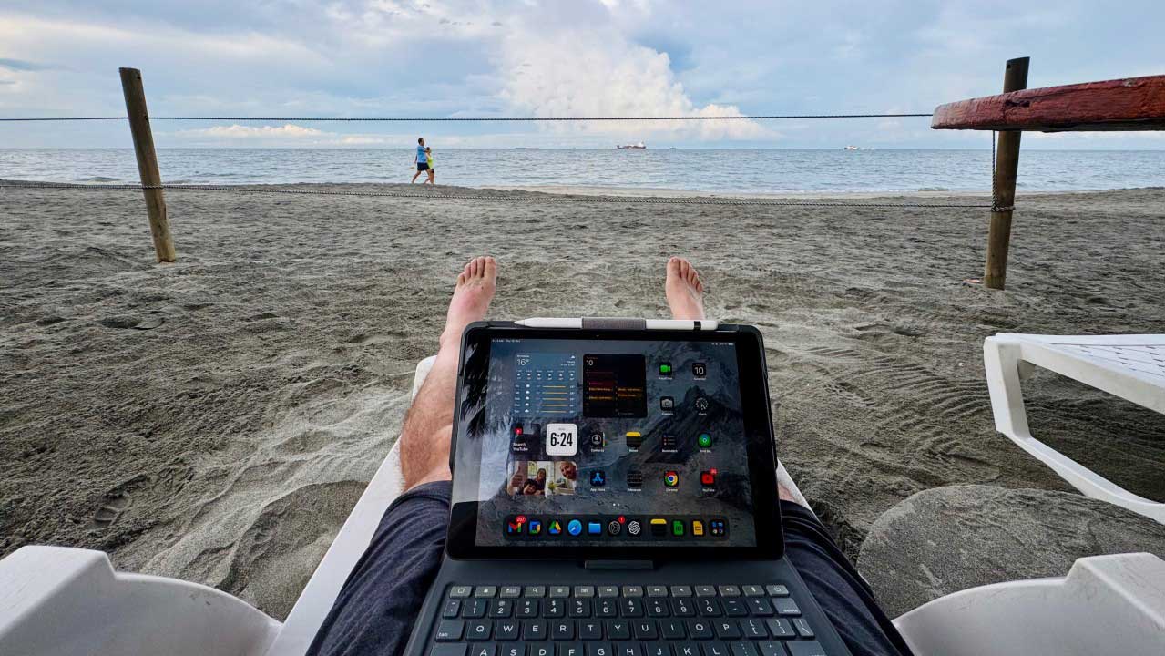 Persona trabajando en la playa con una tablet, disfrutando de vistas al mar