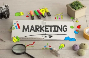 Cuaderno con la palabra marketing rodeado de íconos coloridos que representan crecimiento, comunicación digital y es alusiva a una campaña de marketing